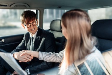 Resmi giysiler içinde çalışan genç bir işadamı, bir kadın ve bir adamın resmi belgeleri olan bir arabada oturması.