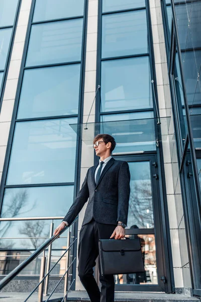 Confident male businessman in a business suit, posing outdoors with an office building in the background