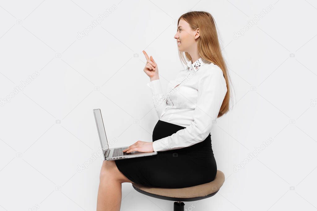 Image of a young pregnant businesswoman in glasses, a girl holding a laptop and pointing to an empty space in the background, sitting on a chair, on a white background