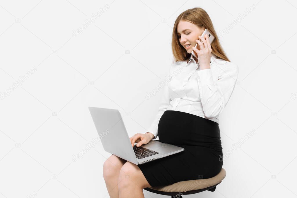 Image of a young pregnant businesswoman in glasses, a girl talking on the phone and working with a laptop, sitting on a chair, on a white background