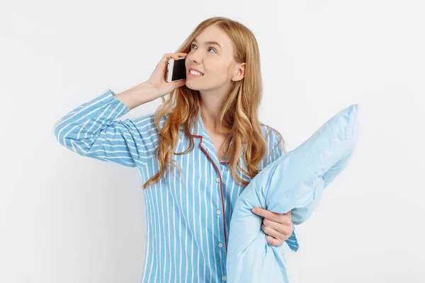 幸せな魅力的な若いです女の子でパジャマとともに枕笑顔上の電話上の白い背景 — ストック写真