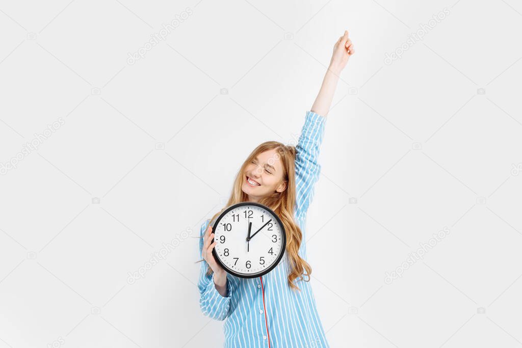 Happy cheerful girl in pajamas, holding a watch, woke up in the morning in a good mood, on a white background