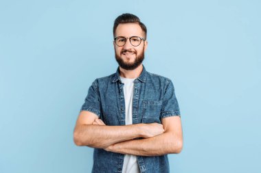 Çekici, gözlüklü, sıradan elbiseli, mavi arka planda duran zeki bir adam.