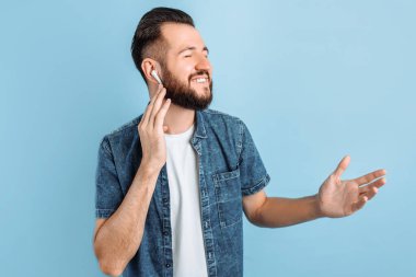 Ayrıca müzik ya da radyo dinleyen gülümseyen bir gencin portresi izole edilmiş mavi arka planda duran modern kablosuz kulaklıklar kullanıyor.