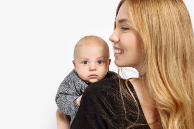 Güzel, şık bir anne, Stüdyo 'da kucağında küçük bir çocuk tutuyor. Siyah elbiseli, uzun, sağlıklı saçlı, şık bir kadın. Beyaz bir arkaplanda izole edilmiş