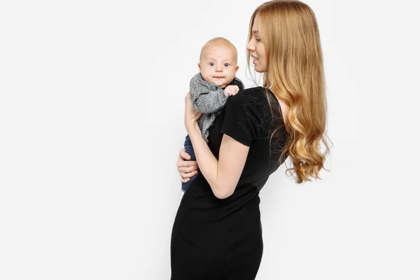 美しいスタイリッシュな母親は スタジオで彼女の腕の中で小さな新生児を保持しています 健康的な髪の長い黒のドレスで美しいファッショナブルな女性 白い背景に隔離された — ストック写真