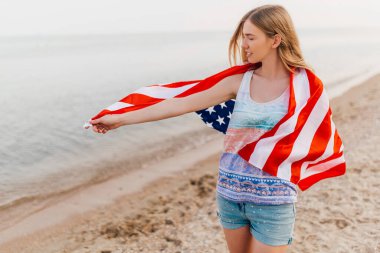 Sahilde elinde Amerikan bayrağı olan ve eğlenen mutlu bir kadın.