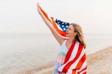 Sahilde elinde Amerikan bayrağı olan ve eğlenen mutlu bir kadın.