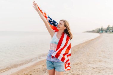Sahilde elinde Amerikan bayrağı olan ve eğlenen mutlu bir kadın.
