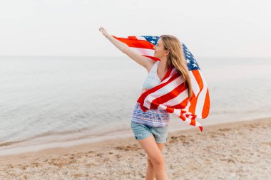 Mutlu bir kadın kumsalda elinde bir Amerikan bayrağıyla eğleniyor.