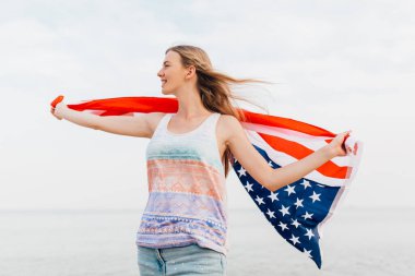 Güzel, vatansever, mutlu bir kadın. Elleri kumsalda duran bir Amerikan bayrağı taşıyor.