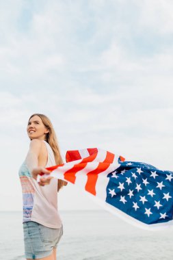 Güzel, vatansever, mutlu bir kadın. Elleri kumsalda duran bir Amerikan bayrağı taşıyor.