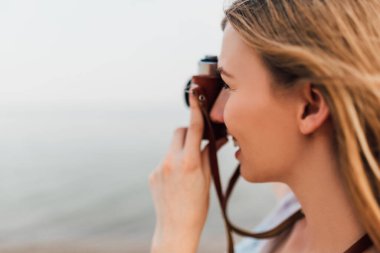 Yakın plan, elinde retro kamera olan, kumsalda eğlenen, güneş gözlüğü takan güzel bir kadının portresi..