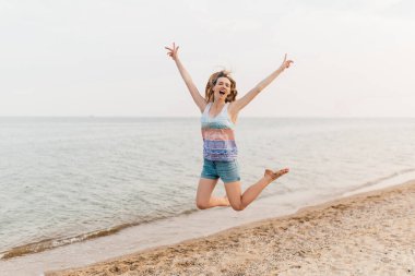 Heyecanlı mutlu kız eğleniyor ve sahilde zıplıyor.