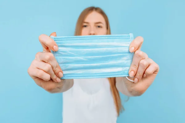 A young girl holds a hygiene mask against infectious diseases, a coronavirus to prevent infection, on an isolated blue background