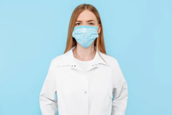 Młoda Lekarka Maską Medyczną Twarzy Białym Fartuchem Odizolowanym Niebieskim Tle — Zdjęcie stockowe
