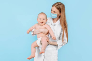Tıp, sağlık ve pediatri konsepti, dijital kızılötesi termometresi olan kadın bir çocuk doktoru, bebeğin vücut ısısını izole edilmiş mavi bir arka planda ölçer.