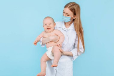 Tıp, sağlık ve pediatri konsepti, dijital kızılötesi termometresi olan kadın bir çocuk doktoru, bebeğin vücut ısısını izole edilmiş mavi bir arka planda ölçer.