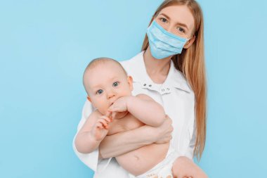 Tıp, sağlık ve pediatri konsepti, dijital kızılötesi termometresi olan kadın bir çocuk doktoru, bebeğin vücut ısısını izole edilmiş mavi bir arka planda ölçer.