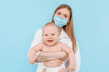 Tıp, sağlık ve pediatri konsepti, dijital kızılötesi termometresi olan kadın bir çocuk doktoru, bebeğin vücut ısısını izole edilmiş mavi bir arka planda ölçer.