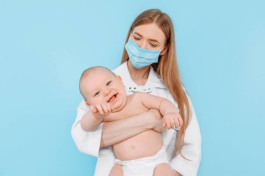 Tıp, sağlık ve pediatri konsepti, dijital kızılötesi termometresi olan kadın bir çocuk doktoru, bebeğin vücut ısısını izole edilmiş mavi bir arka planda ölçer.