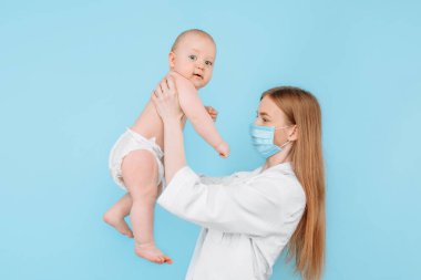 Tıp, sağlık ve pediatri konsepti, dijital kızılötesi termometresi olan kadın bir çocuk doktoru, bebeğin vücut ısısını izole edilmiş mavi bir arka planda ölçer.