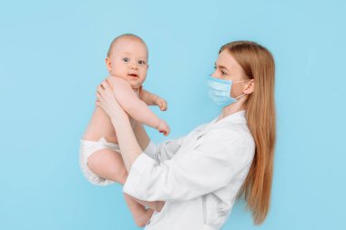 Tıp, sağlık ve pediatri konsepti, dijital kızılötesi termometresi olan kadın bir çocuk doktoru, bebeğin vücut ısısını izole edilmiş mavi bir arka planda ölçer.