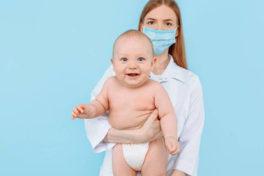 Tıp, sağlık ve pediatri konsepti, dijital kızılötesi termometresi olan kadın bir çocuk doktoru, bebeğin vücut ısısını izole edilmiş mavi bir arka planda ölçer.