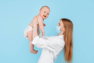Tıp, sağlık ve pediatri konsepti, dijital kızılötesi termometresi olan kadın bir çocuk doktoru, bebeğin vücut ısısını izole edilmiş mavi bir arka planda ölçer.