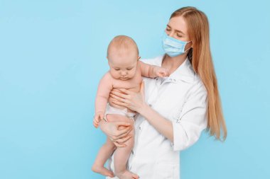 Tıp, sağlık ve pediatri konsepti, dijital kızılötesi termometresi olan kadın bir çocuk doktoru, bebeğin vücut ısısını izole edilmiş mavi bir arka planda ölçer.