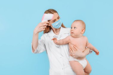 Tıp, Sağlık ve Pediatri konsepti. İzole edilmiş mavi arka planda bebeğin alnının sıcaklığını ölçen dijital kızılötesi termometresi olan kadın bir çocuk doktoru.