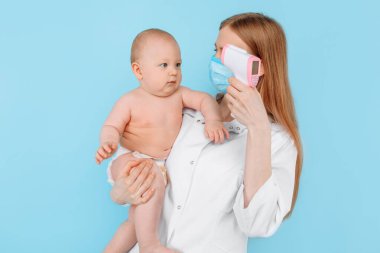 Tıp, Sağlık ve Pediatri konsepti. İzole edilmiş mavi arka planda bebeğin alnının sıcaklığını ölçen dijital kızılötesi termometresi olan kadın bir çocuk doktoru.