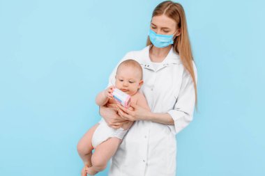 Tıp, Sağlık ve Pediatri konsepti. İzole edilmiş mavi arka planda bebeğin alnının sıcaklığını ölçen dijital kızılötesi termometresi olan kadın bir çocuk doktoru.