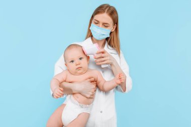 Tıp, Sağlık ve Pediatri konsepti. İzole edilmiş mavi arka planda bebeğin alnının sıcaklığını ölçen dijital kızılötesi termometresi olan kadın bir çocuk doktoru.