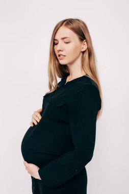 Siyah elbiseli güzel hamile kadın beyaz arka planda poz veriyor, moda fotoğrafçısı hamileliği.