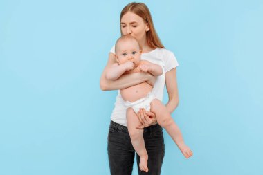 Mutlu bir anne ve bebek bezi takmış küçük bir çocuk, soyutlanmış mavi bir arka planda birlikte eğlenen bir aile.