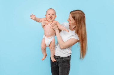 Mutlu bir aile. Gülen bir anne, sevimli yeni doğan oğlunu mavi bir arka plana nazikçe kaldırır.