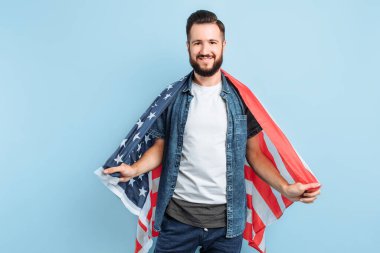 Bağımsızlık Günü kutlaması. Yıldızlar ve çizgiler. Amerika Birleşik Devletleri bayrağına sahip genç bir adam, izole edilmiş mavi bir arka planda, ülkesinin bir vatansever gibi mutlu görünüyor.