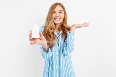 Pijamalı bir kız elinde beyaz plastik bir hap kavanozu, hastalıkların tıbbi tedavisi için bir konsept, beyaz bir arka planda beyaz bir hap kavanozunun yakın çekimi,