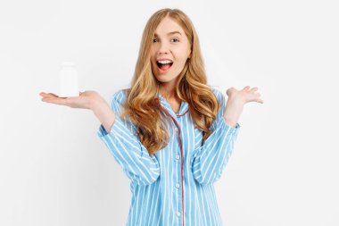 Pijamalı bir kız elinde beyaz plastik bir hap kavanozu, hastalıkların tıbbi tedavisi için bir konsept, beyaz bir arka planda beyaz bir hap kavanozunun yakın çekimi,