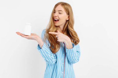 Pijamalı bir kız elinde beyaz plastik bir hap kavanozu, hastalıkların tıbbi tedavisi için bir konsept, beyaz bir arka planda beyaz bir hap kavanozunun yakın çekimi,