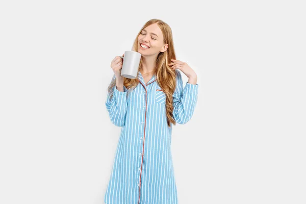 白い背景に 早朝にコーヒーや紅茶を飲んで 彼女の手にカップで 縞模様のパジャマで美しい女の子 — ストック写真