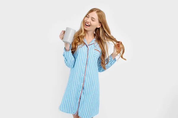 白い背景に 早朝にコーヒーや紅茶を飲んで 彼女の手にカップで 縞模様のパジャマで美しい女の子 — ストック写真