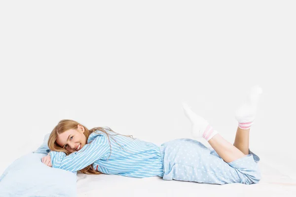白い背景に彼女の手 足を上に枕でベッドの上に横たわって パジャマで美しい女の子 — ストック写真