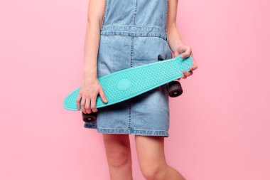 Pembe arka planda kaykay tutan bir kızın yakın çekimi.