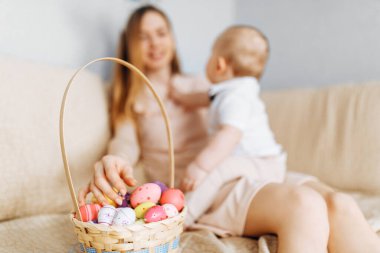 Tavşan kulaklı anne ve bebek sepetinde Paskalya yumurtaları ile kanepede oturuyor, ebeveynler ve çocuklar içeride oynuyor. Aile Paskalyayı kutlar, aile tatili.