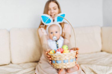 Mutlu Paskalyalar. Paskalya günü tavşan kulaklı bir anne ve küçük bir bebek, Paskalya yumurtası boyalı, eğlen, oyna ve sarıl, kanepede otur. Aile Paskalyayı kutluyor