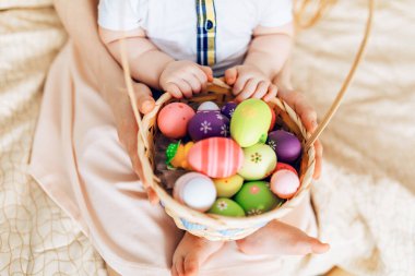 Mutlu Paskalyalar. Mutlu bir anne ve küçük çocukların ellerinde renkli yumurtaları evde bir sepetin içinde tutarken.