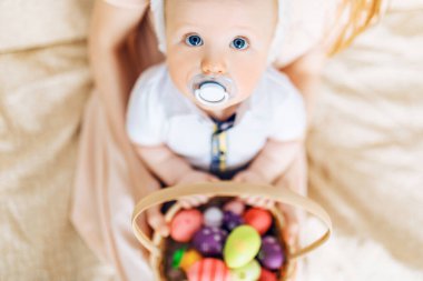 Mutlu Paskalyalar. Paskalya günü tavşan kulaklı bir anne ve küçük bir bebek, Paskalya yumurtası boyalı, eğlen, oyna ve sarıl, kanepede otur. Aile Paskalyayı kutluyor