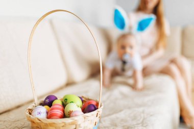 Tavşan kulaklı sevimli bebek evde kanepenin üzerinde paskalya yumurtalarıyla sepete doğru sürünüyor.